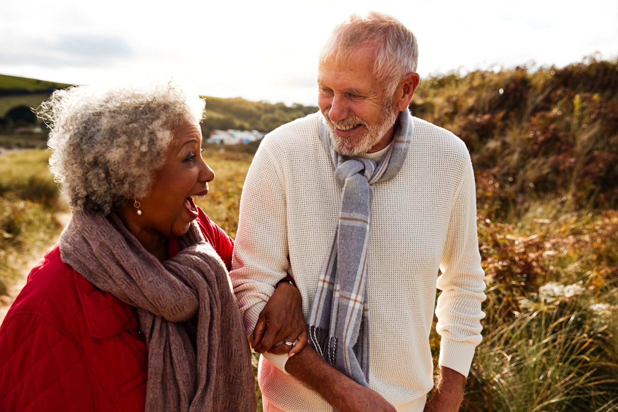 Loving Active Senior Couple Walking Arm In Arm Through Sand Dunes On Winter Beach Vacation